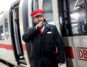 Ein Mann in Deutscher-Bahn-Uniform spricht vor einem Zug in ein Walkie-Talkie.