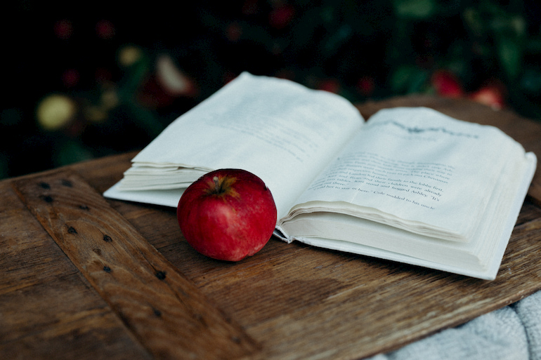 Offenes Buch mit einem Apfel davor.