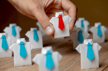 Papiermännchen mit roter Krawatte in Mitten von Papiermännchen mit blauer Krawatte.