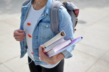 Eine junge Frau mit Rucksack hält Bücher im Arm.