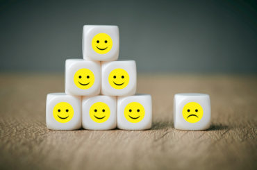 Viele Würfel mit lachenden Smileys und ein Würfel mit einem traurigen Smiley.