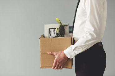 Ein Mann trägt nach seiner Kündigung eine Kiste mit seinen Gegenständen aus dem Büro.