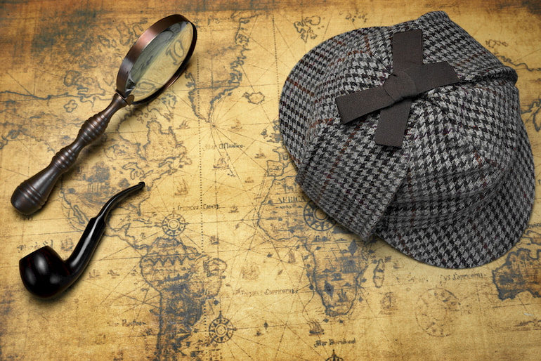 Eine Detektiv-Mütze, eine Lupe und eine Pfeife liegen auf einer alten Karte.