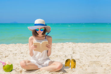Eine Frau sitzt am Strand und liest ein Buch.