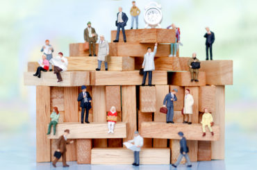 Viele Miniaturfiguren sitzen auf Bauklötzen.