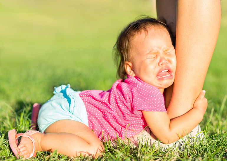 Ein weinendes Baby klammert sich ans Bein seiner Mutter.