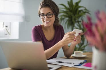 frau haelt smartphone und schaut auf laptop