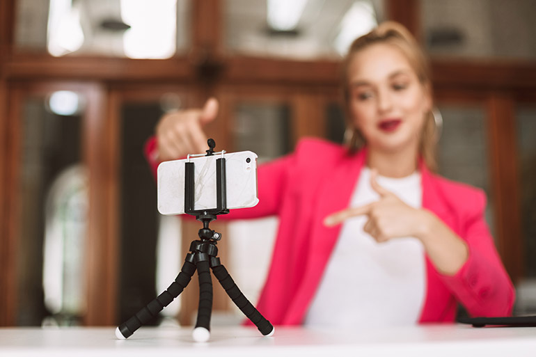 Eine Frau macht ein Selfie-Video mit Smartphone und Stativ.