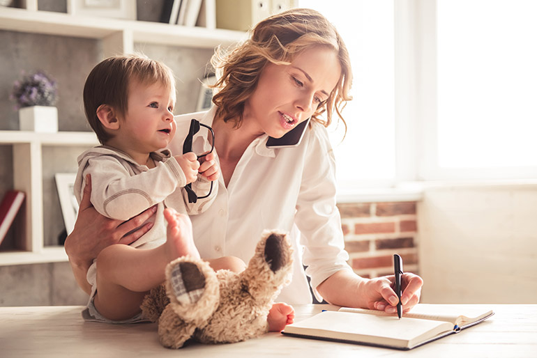 Eine Frau hält ein Baby im Arm, während sie am Telefon einen Termin macht.