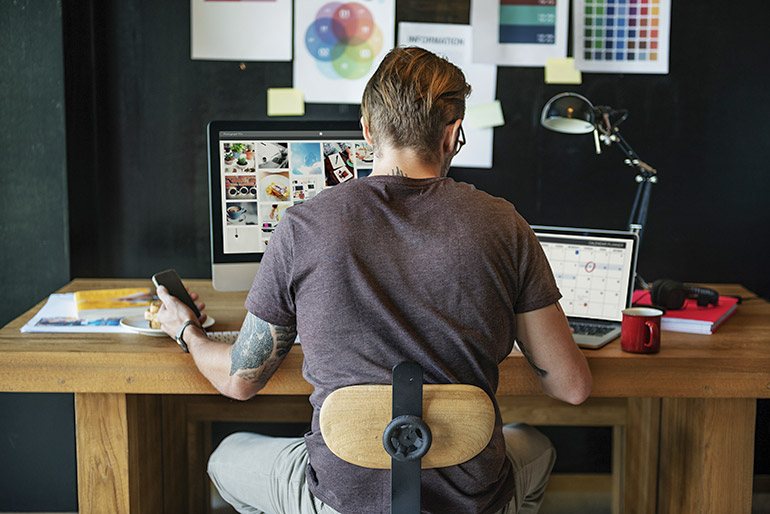 Ein Mann sitzt an einem modernen Schreibtisch und bearbeitet Fotos.