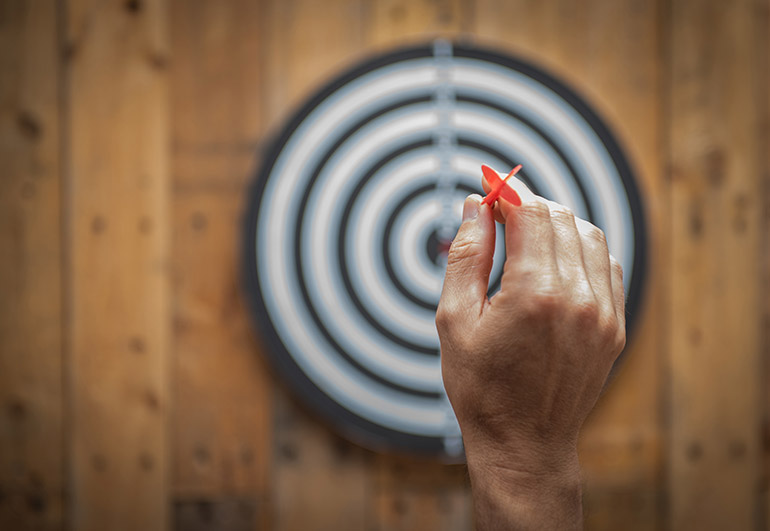 Ein Mann zielt mit einem Pfeil auf eine Dartscheibe.