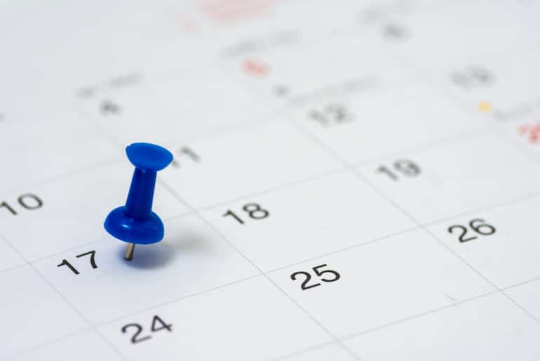 Eine blaue Stecknadel steckt in einem Termin in einem Kalender.