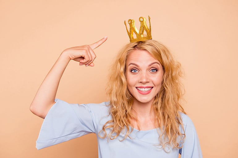 Eine Frau zeigt auf die Krone, die sie auf dem Kopf trägt.