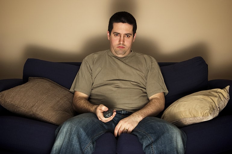 Ein Mann sitzt gelangweilt auf der Couch und schaut Fernsehen.