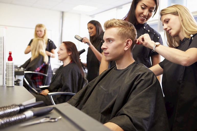 Eine Friseurin unterrichtet eine Azubine beim Haareschneiden.