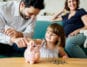 Mutter und Vater sehen Kind dabei zu, wie es Geld in ein Sparschwein tut.