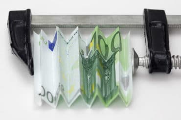 Symbolbild: Ein 100-Euro-Schein, eingespannt in einem Schraubstock.