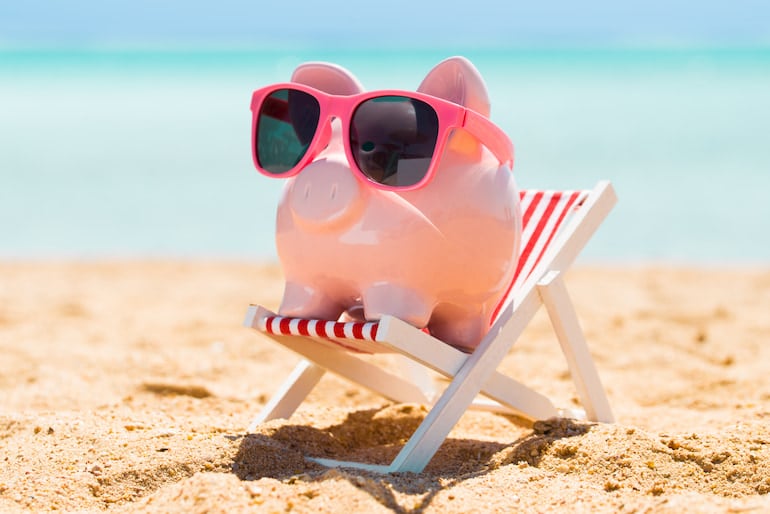 Urlaubsgeld: Ein Sparschwein sitzt in einem Liegestuhl am Meer.
