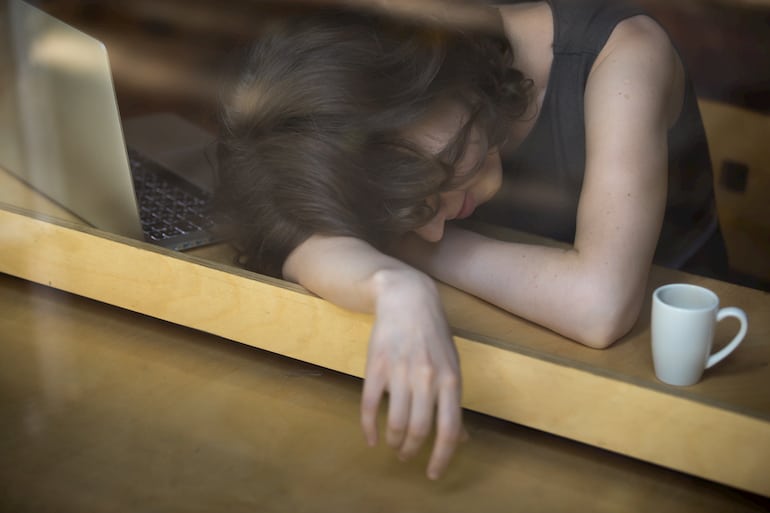 Junge Frau schläft bei der Nachtarbeit neben ihrem Notebook ein