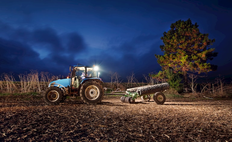 Landwirt verrichtet Nachtarbeit auf von Traktor beleuchtetem Feld