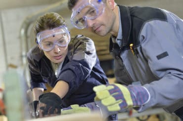 Auszubildende schleift Holz mit Anleitung vom Ausbilder