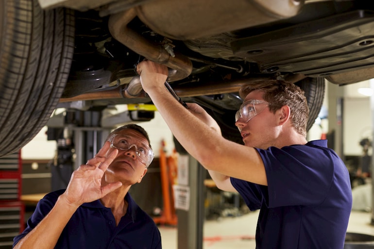 Auszubildender bekommt Tipps zur Reparatur eines Auspuffs während der Ausbildung