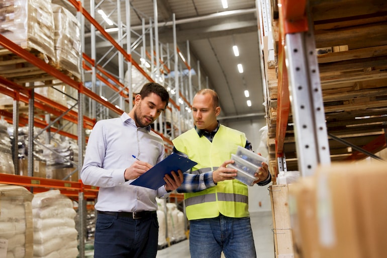 Ein Industriekaufmann prüft mit einem Lagermitarbeiter die Bestände in der Lagerhalle