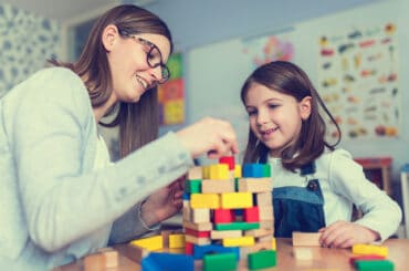 Kinderpfleger und Mädchen spielen mit Bauklötzen