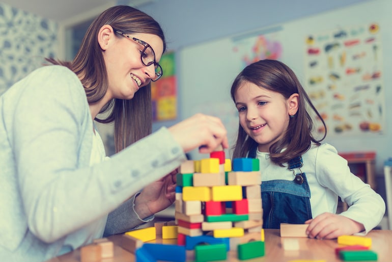 Kinderpfleger und Mädchen spielen mit Bauklötzen