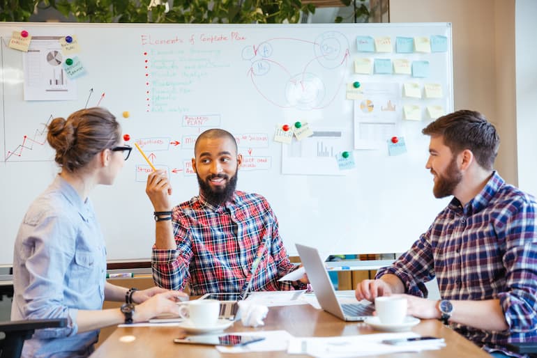 Drei Arbeitnehmer sitzen an einem tisch und arbeiten nach dem New-Work-Prinzip zusammen an einem Projekt