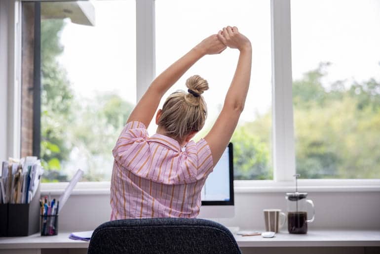 Eine Frau sitzt vor dem Computer und macht Rückenübungen am Arbeitsplatz