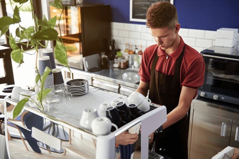 Ein Schüler hat einen Ferienjob in der Gastronomie und macht Kaffee in einem Café